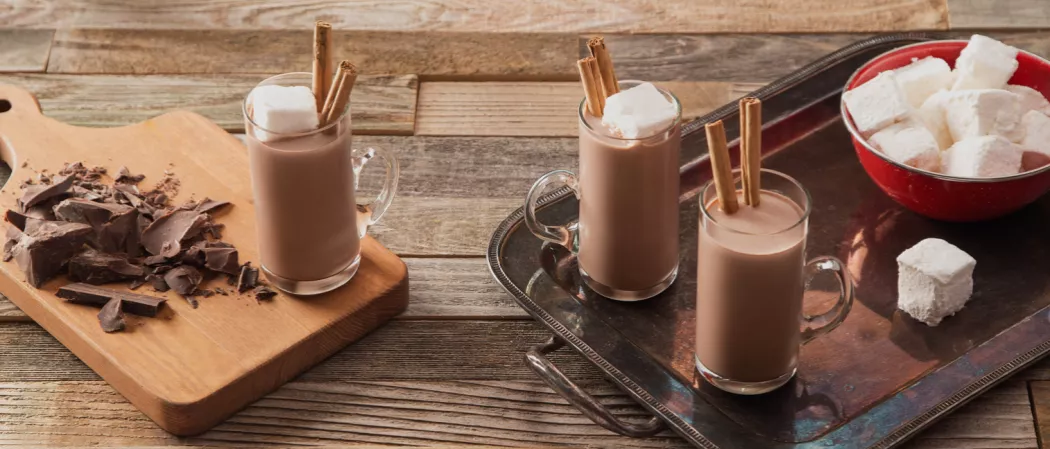 Three Fireside Coco glasses: two with a bowl of marshmallows on a tray, one with chopped chocolate on a board