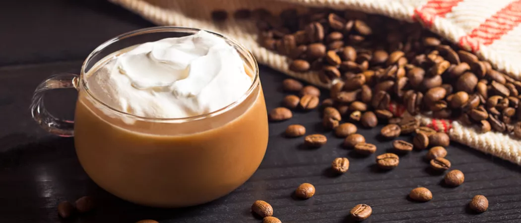 Cup of Kentucky Coffee garnished with whipped cream alongside coffee beans