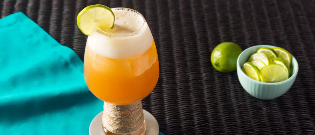 Glass of Slowpoke Shandy garnished with lime slice alongside bowl of lime slices and a lime