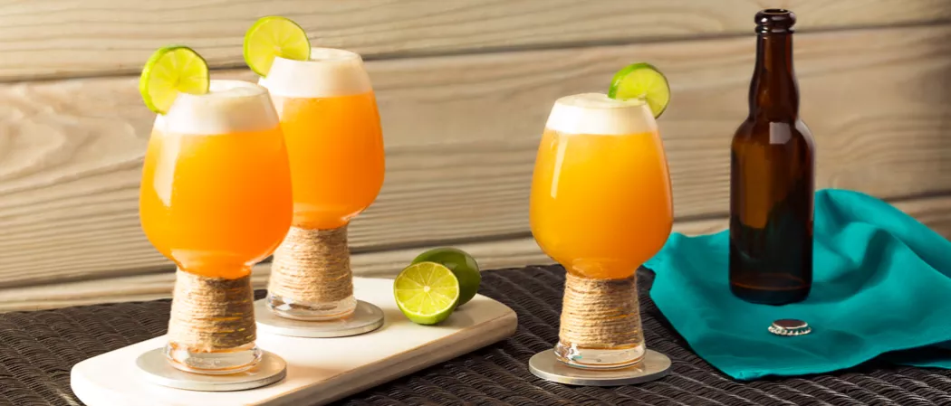 Three glasses of Slowpoke Shandy garnished with lime slices two on white board with limes