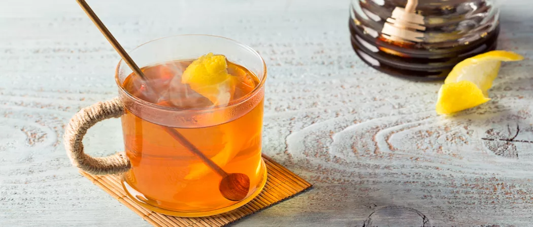 Cup of Hot Toddy garnished with lemon peel with a wooden spoon