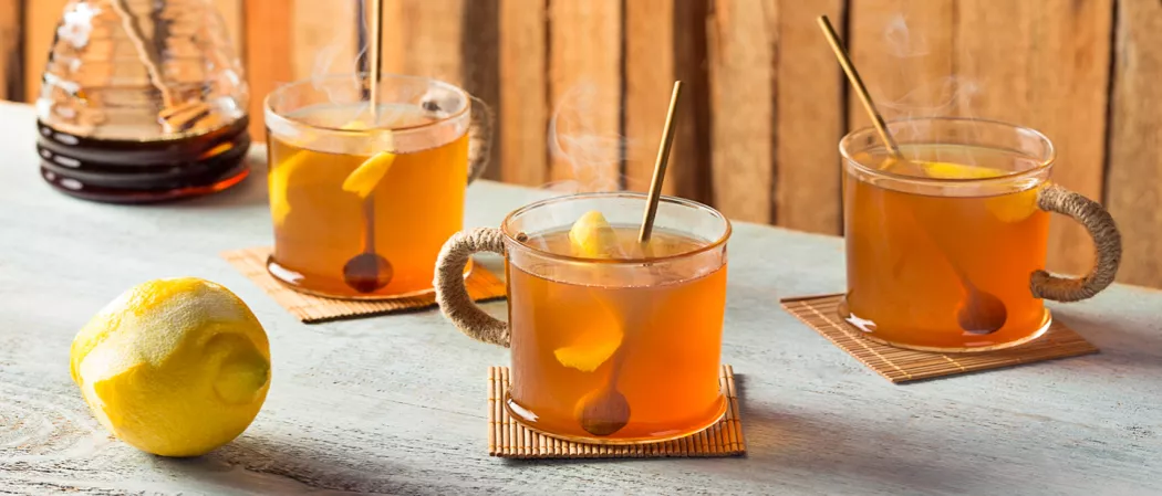 Three cups of Hot Toddy garnished with lemon peel and wooden spoon alongside a lemon