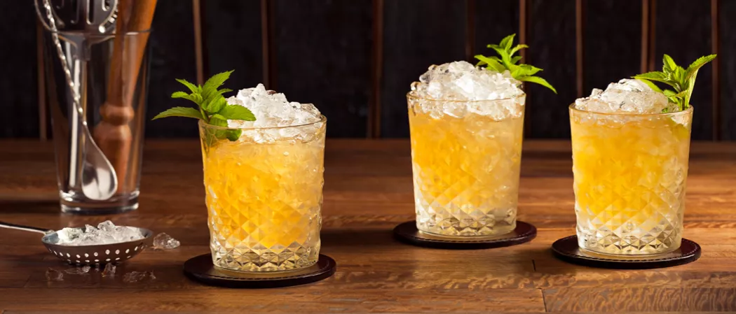 Three Double Oak Whiskey Smash glasses on coasters, filled with crushed ice, mint leaves garnish, and a ladle with more ice