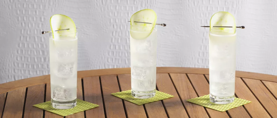 Three glasses of EFFEN® Green Apple Cooler garnished with apple slice on green coasters.