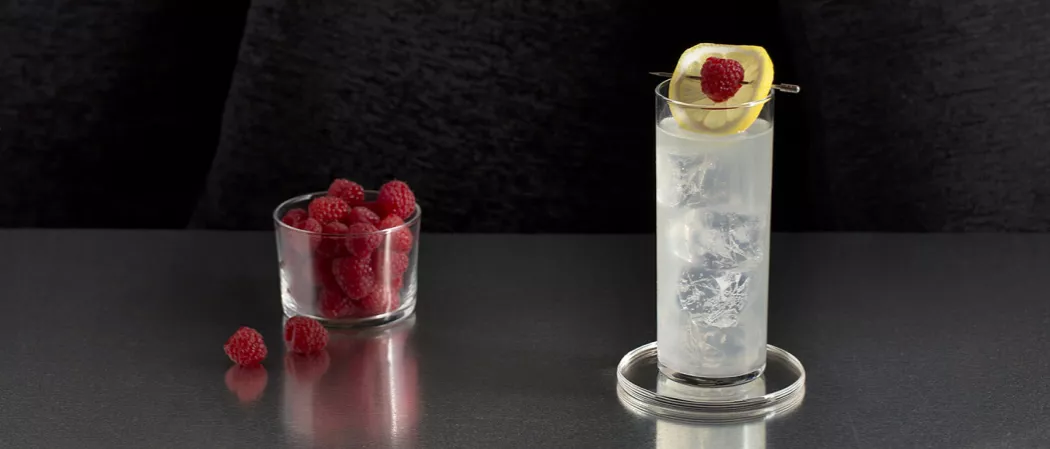 Glass of EFFEN® Raspberry Lemonade garnished with lemon slice and raspberry on glass coaster alongside a bowl of raspberries