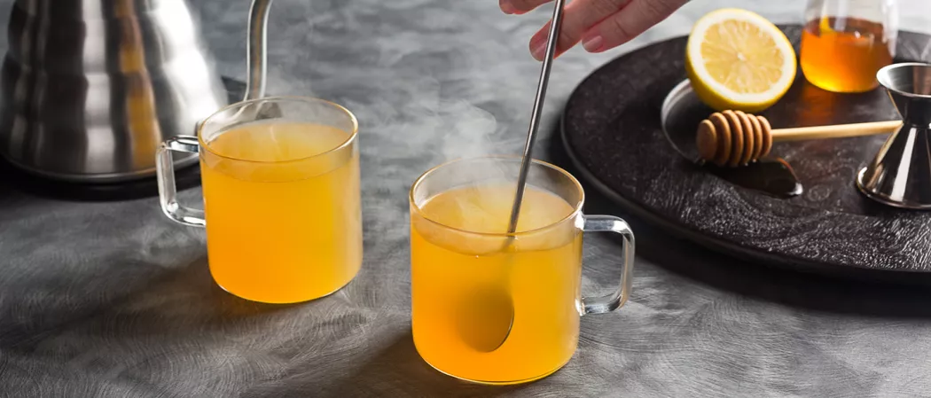person stirring cup of Jim Beam® Black Hot Toddy using bar spoon alongside another glass of Jim Beam® Black Hot Toddy 
