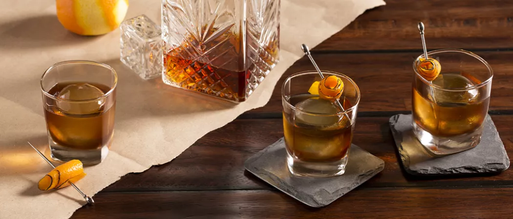 two glasses of Rye Opener garnished with orange peel on coaster alongside another glass of Rye Opener and orange peel