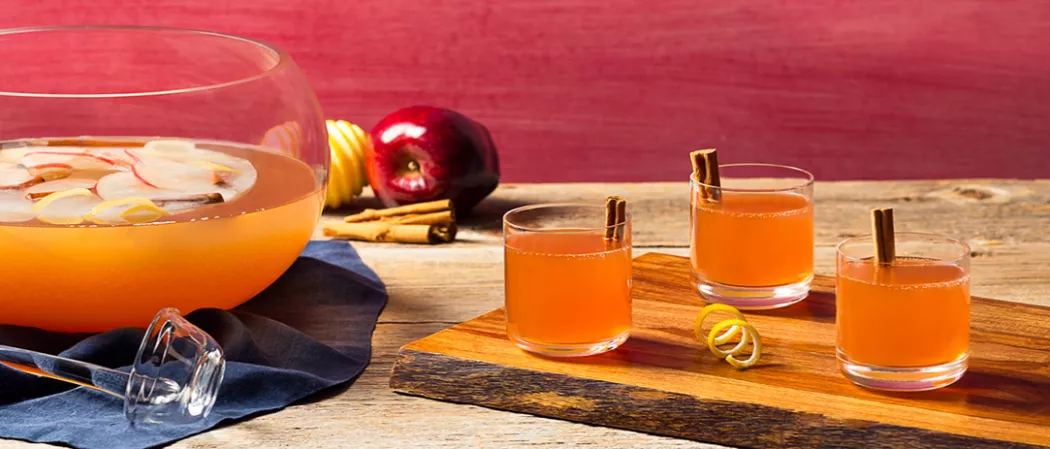 Three Glasses of Spiced Christmas Punch garnished with cinnamon stick on wooden board alongside a lemon peel twist