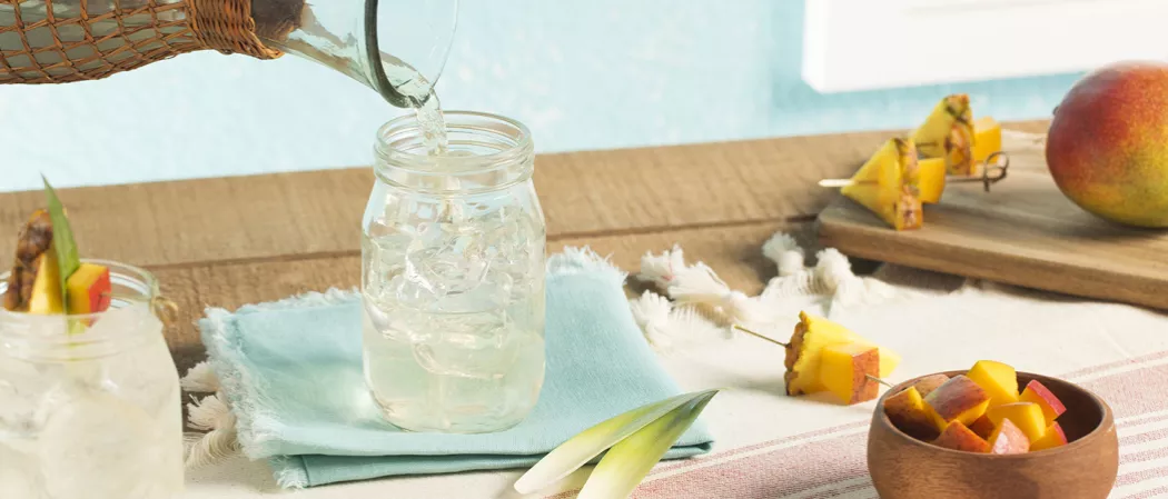 One Cruzan® Confusion with pineapple, pineapple leaves, and mango garnish, while the other glass is being prepared with garnishing items on the table, including chopped mango in a small bowl.