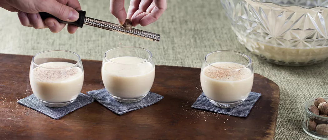 Person grating nutmeg into glass of Yule Nog