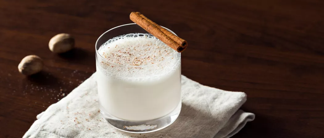 Glass of Bourbon Milk Punch on a napkin, garnished with a cinnamon stick.