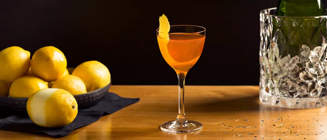 Glass of Kiss Me Cocktail alongside some lemons and a glass