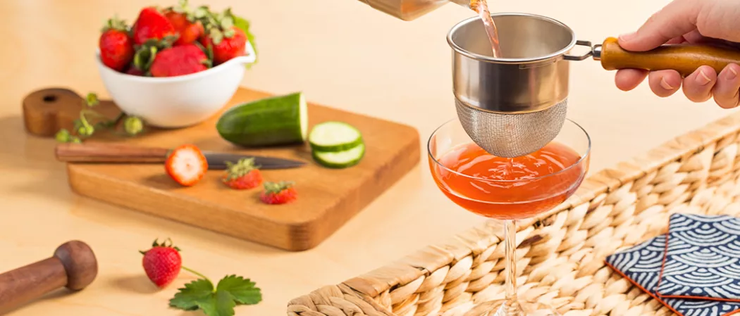 Person straining Melon Berry Mist into cocktail glass