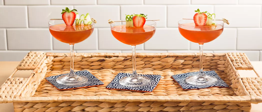 Three glasses of Melon Berry Mist garnished with th strawberry and cucumber wheel on coaster on wooden knit tray