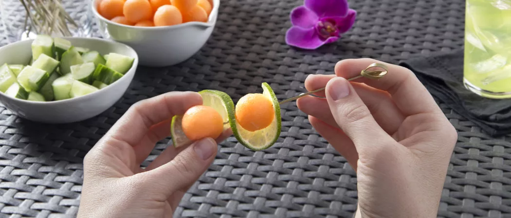 Person creating melon ball and lime slice garnish