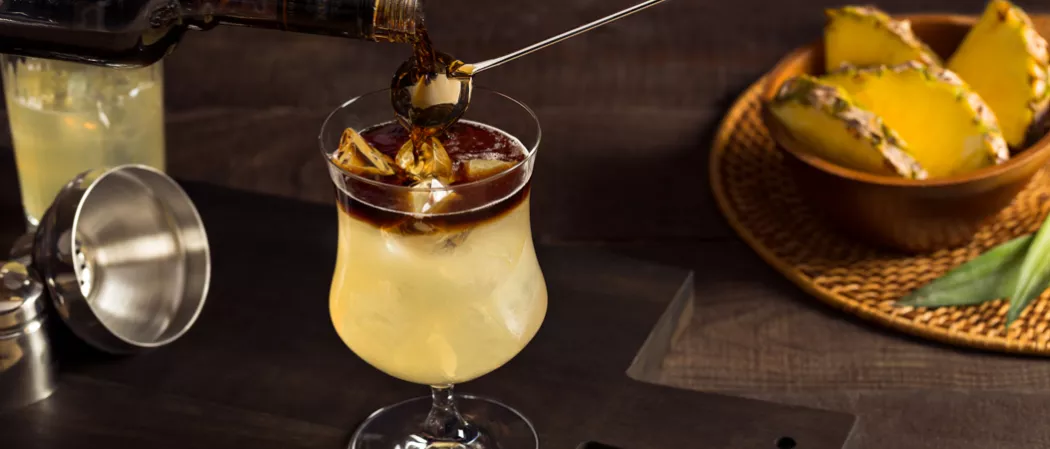 Pouring Cruzan® Mai Tai into glass alongside bowl of pineapple wedges