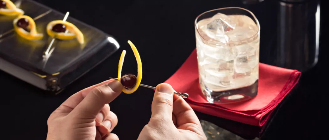 Person creating brandied cherries garnish alongside glass of Vodka Beast