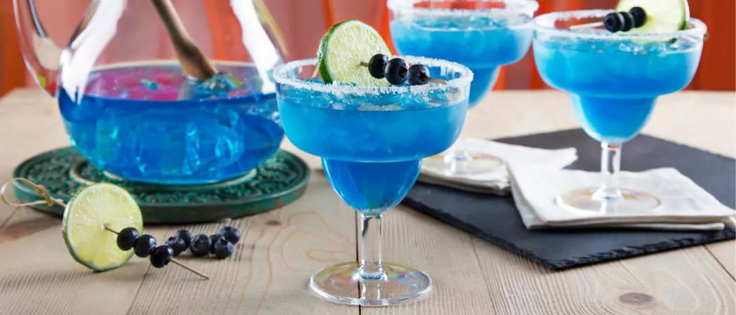 Three glasses of  Blue Margarita garnished with Lime, Blueberries and Salt  and bowl full of Blue Margarita