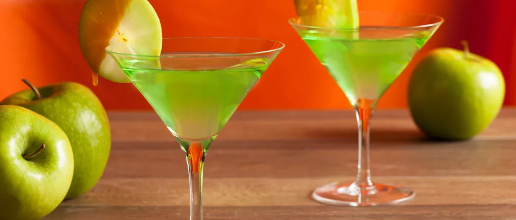 Two glasses of Caramel Apple Martini garnished with an apple wheel, alongside some additional apples