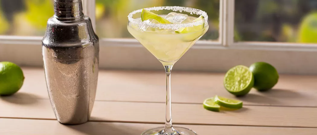 A glass of Sauza® Classic Margarita garnished with lemon slices and salt alongside a shaker and few lime and lime slices