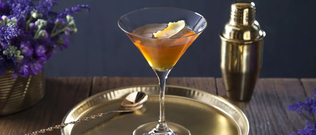 Glass of Courvoisier® Sidecar on bronze plate alongside a bar spoon and a shaker