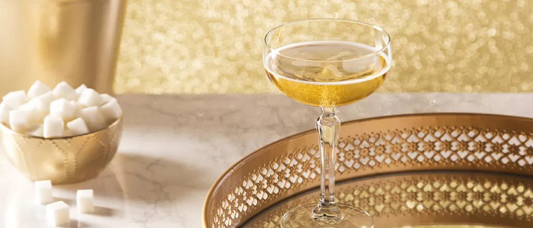 Glass of Sparkling Cognac garnished with pineapple wedge and leaf alongside a half pineapple