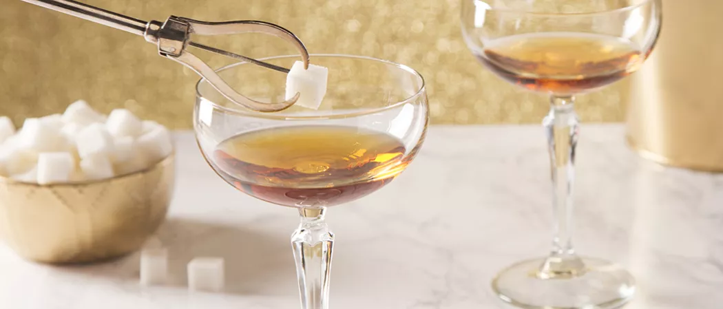 Three Glasses of Sparkling Cognac garnished with pineapple wedge and leaf one on wooden board alongside shaker and strainer in glass