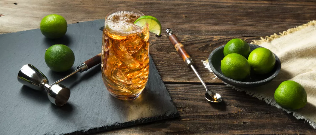 A glass of Cruzan® Safe Harbor garnished with  Lime Wedge along with lime on the table and in a bowl