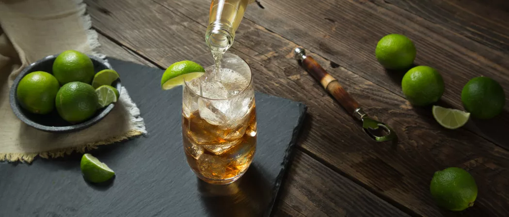 A person pouring Fever-Tree Ginger Beer along with chopped lime on the table and some lime in a bowl