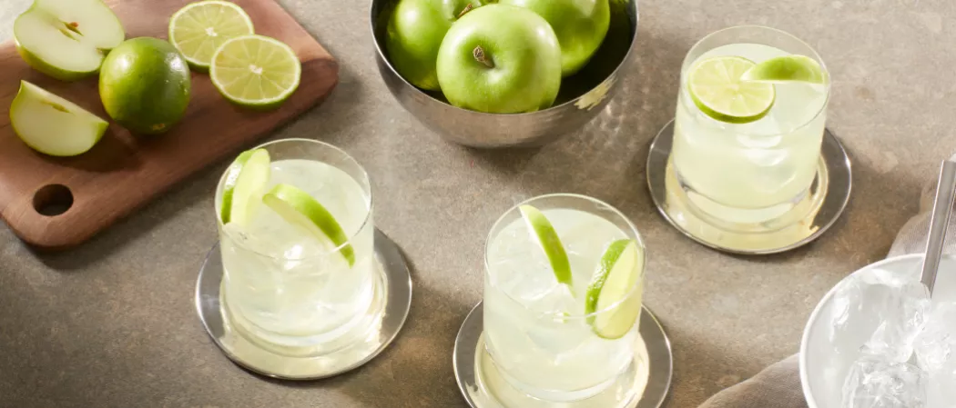 Three  glasses of DeKuyper® End of the Rainbow garnished with Green Apple Slices and Lime Wheel along with bowl of green apple