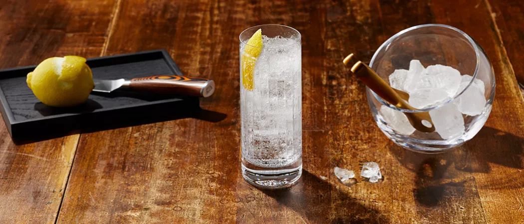 A glass of Haku® Highball (“Haku-Hi”) garnished with lemon peel along with cup of ice cubes and  half peeled lemon