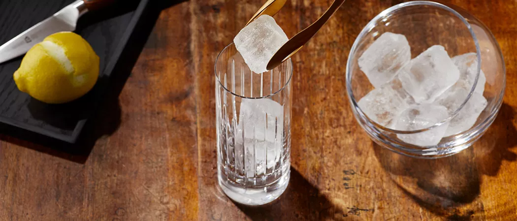 A glass of Haku® Highball (“Haku-Hi”) garnished with lemon peel along with cup of ice cubes and  half peeled lemon