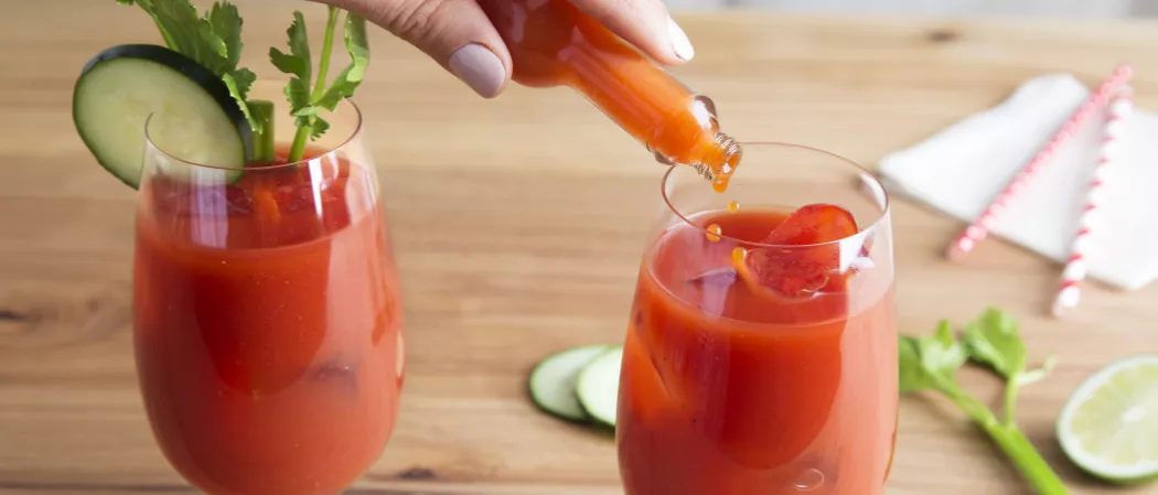 A person pouring DashWorcestershire sauce into a glass of Skinnygirl® Bloody Mary and one more glass is there of Skinnygirl® Bloody Mary