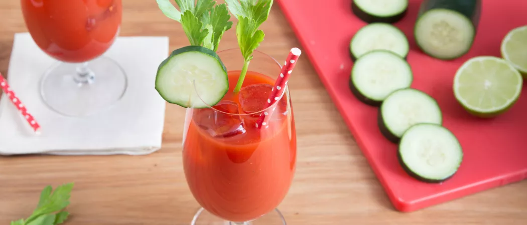 A glass of Skinnygirl® Bloody Mary garnished with Cucumber Slices , mint leaves and a straw