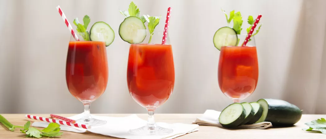 Three glasses of Skinnygirl® Bloody Mary garnished with Cucumber Slices , mint leaves and a straw along with chopped cucumber