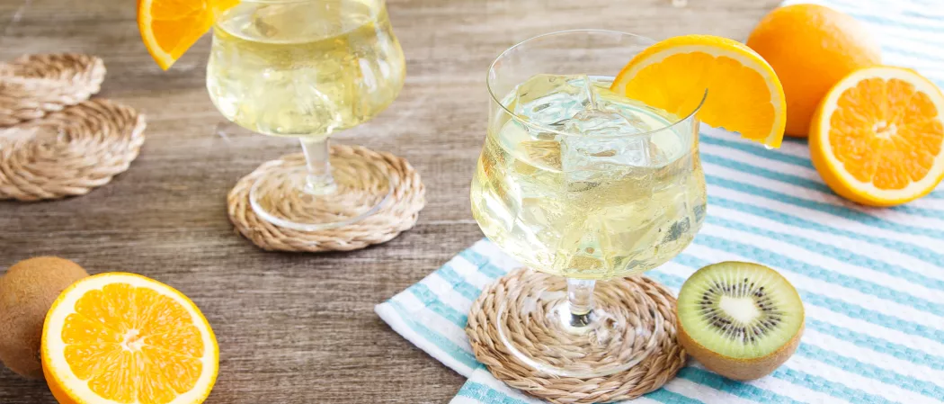 Two glasses of Cruzan® Daiquiri garnished with orange wedge alongside some half oranges and kiwi