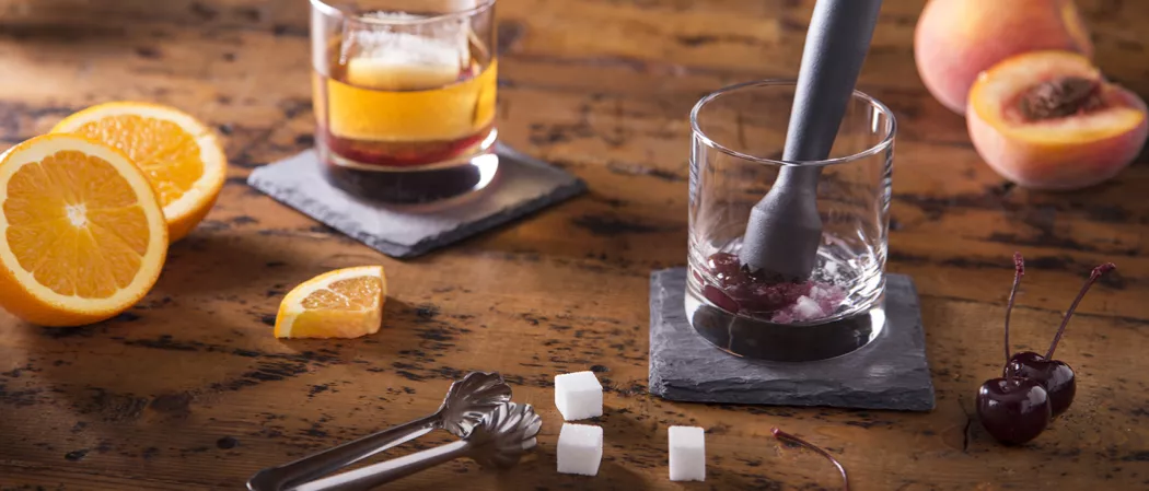 Person crushing cherry into glass using muddle