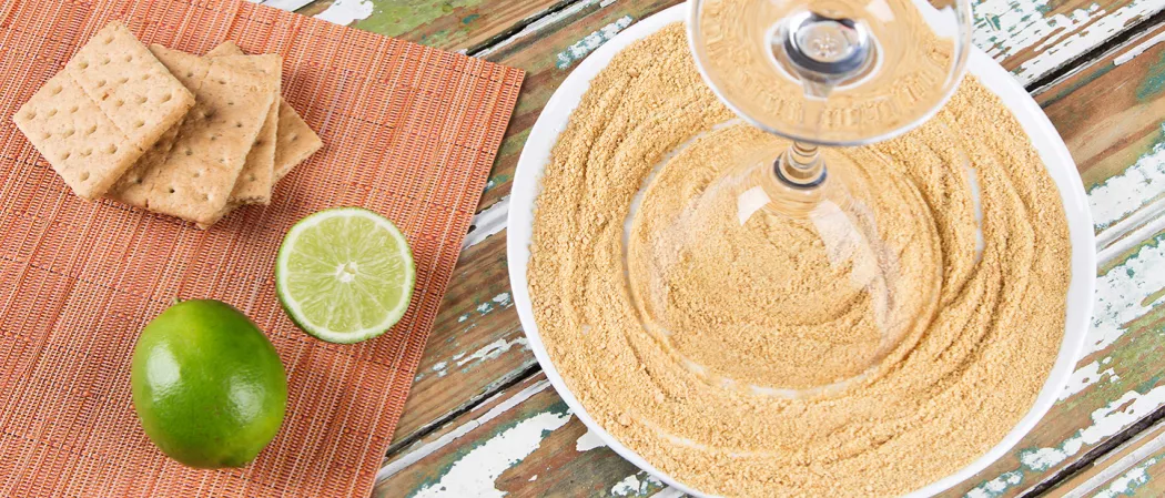 Inverted glass on a plate of crushed graham crackers, alongside a few crackers and one and a half lime.
