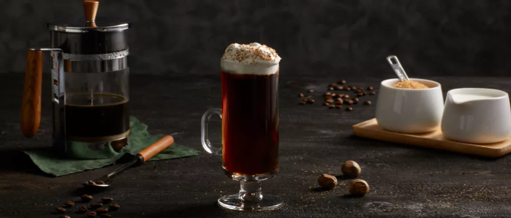 A glass of  Kilbeggan® Irish Coffee garnished with Whipped heavy cream and Grated Nutmeg along with Brown Sugar Syrup