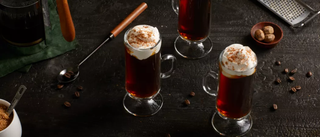 Three glasses of  Kilbeggan® Irish Coffee garnished with Whipped heavy cream and Grated Nutmeg 