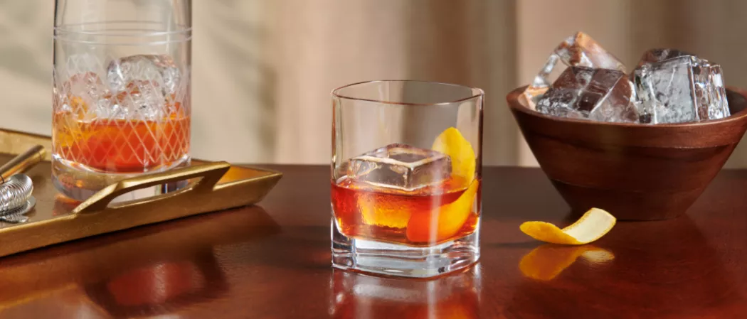 Glass of Knob Creek® Old Fashioned garnished with lemon peel alongside a lemon peel and a bowl of ice.