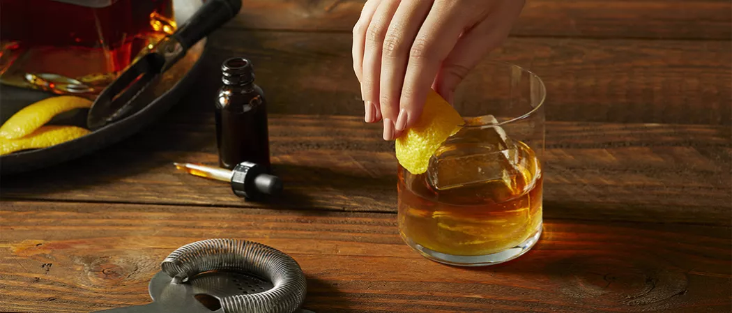 A person garnishing lemon peel on glass of Knob Creek® Rye Old Fashioned along with strainer and Angostura® Bitters