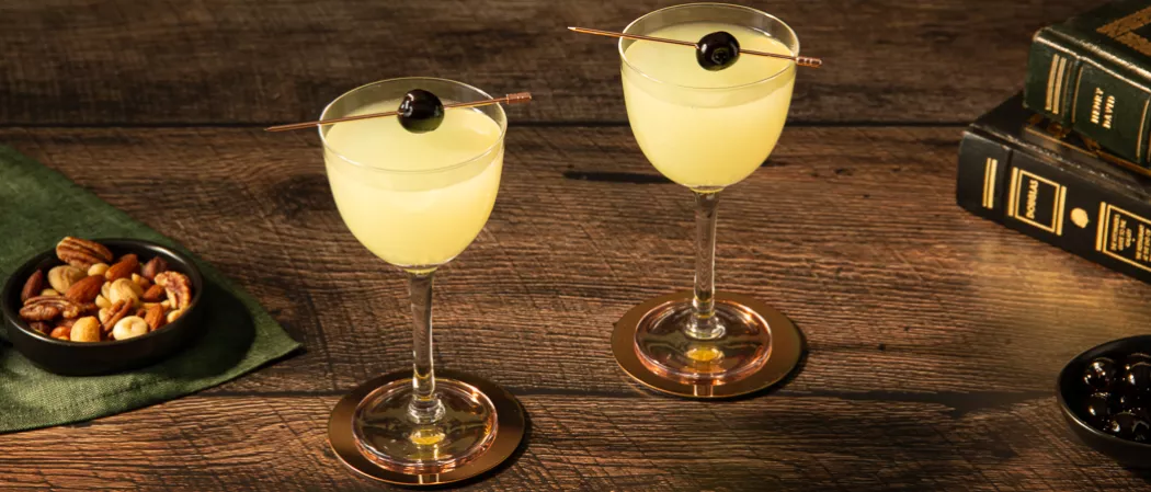 Two glasses of Last Word garnished with black cherries along with the small dry fruits bowl on a green cloth