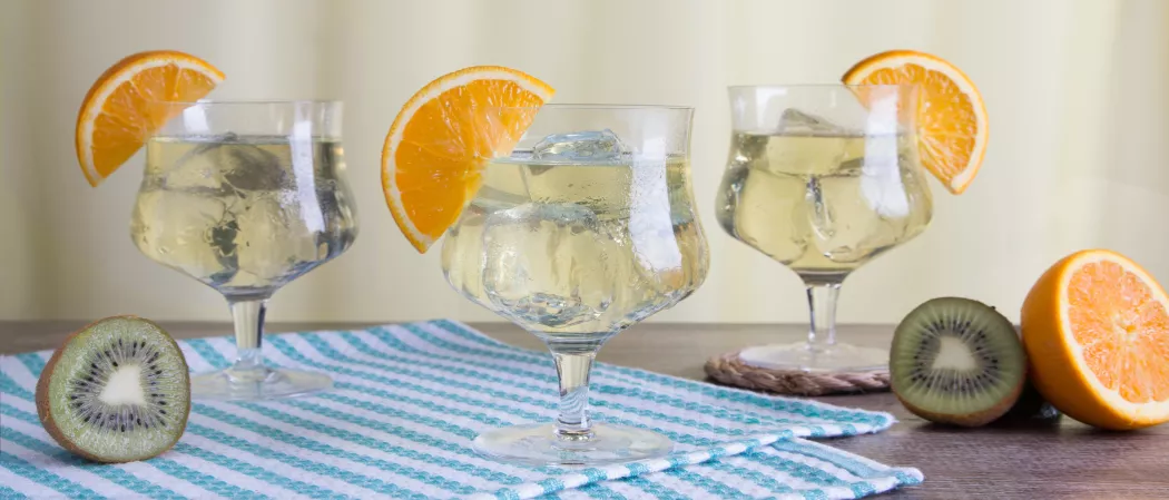 three glasses of Cruzan® Daiquiri garnished with orange wedge alongside some half kiwis and orange