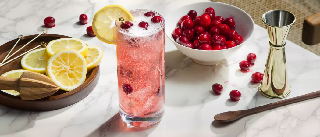 A glass of Maker's Mark® Merry Berry Buck garnished with Cranberries and lemons along with bowl of cranberries and chopped lemons
