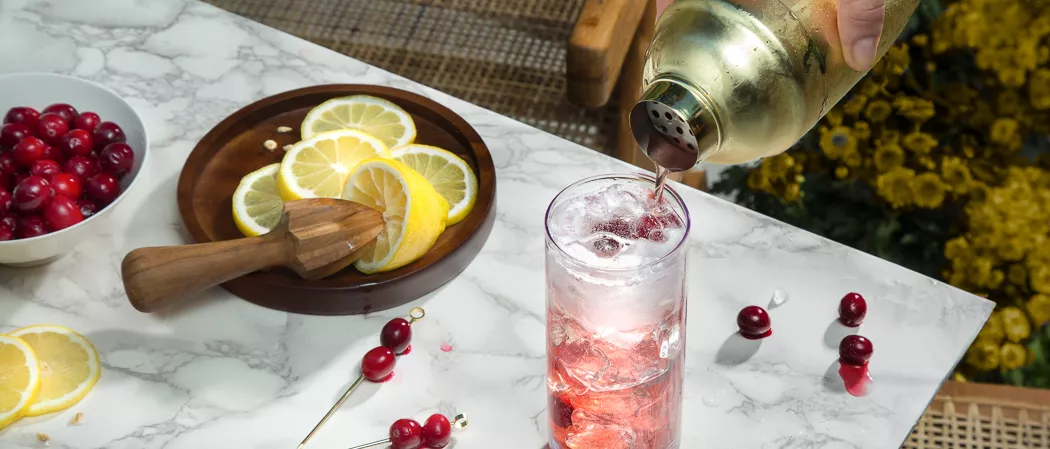 A person pouring Fever-Tree Ginger Beer into a glass of Maker's Mark® Merry Berry Buck along with chopped lemons