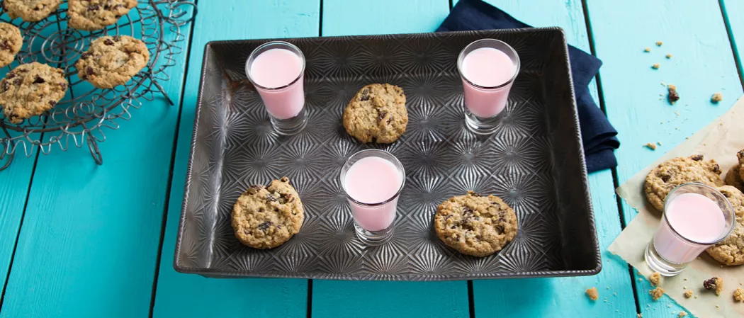 Three glasses of Oatmeal Cookie, each with three cookies on a black tray on a blue cloth. Few cookies on another tray. One glass with a few cookies on paper