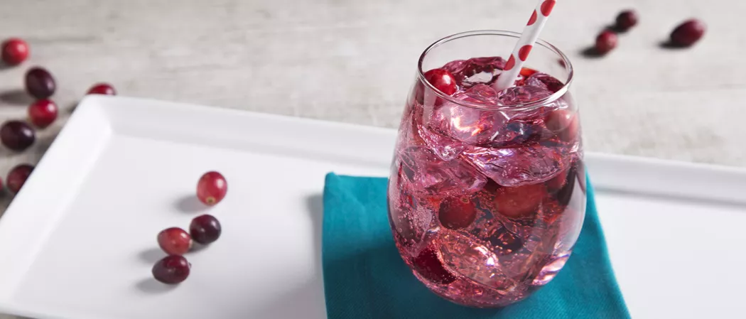 A glass of flirty fizz cocktail with ice and a straw on blue coaster