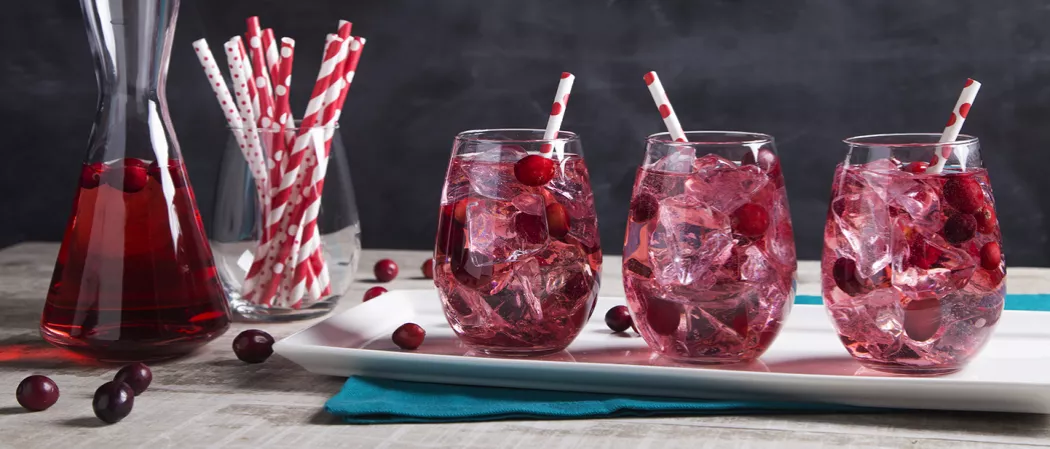 Three glasses of fizz cocktail with ice and a straw alongside a glass of straws