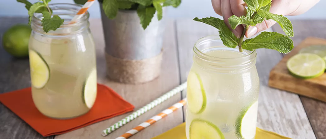 A person garnishing jar of Handsome Ginger with mint leaves alongside another jar of same garnished with mint leaves, lime slices and straws.